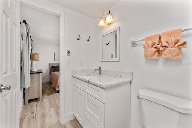 ensuite bathroom with connected bathroom, toilet, vanity, and wood finished floors