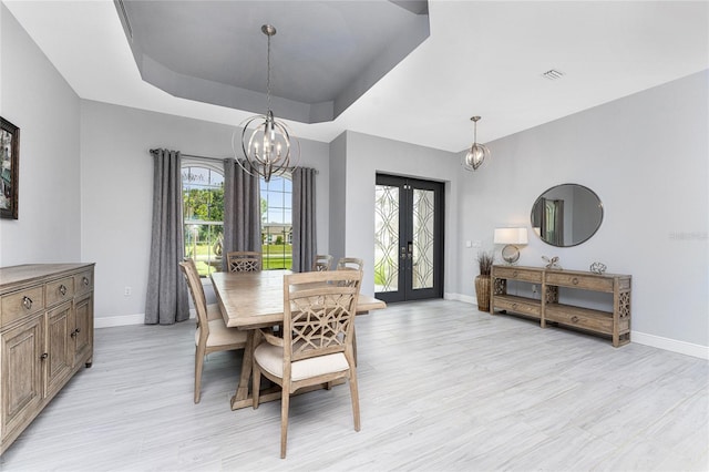 dining room with an inviting chandelier, a raised ceiling, light hardwood / wood-style flooring, and french doors