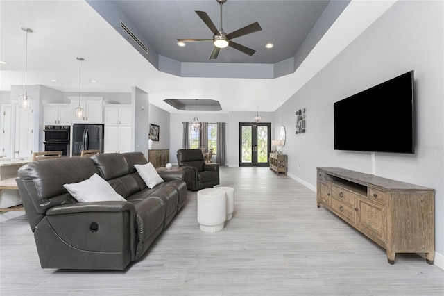 living room featuring ceiling fan, light hardwood / wood-style floors, a raised ceiling, and french doors