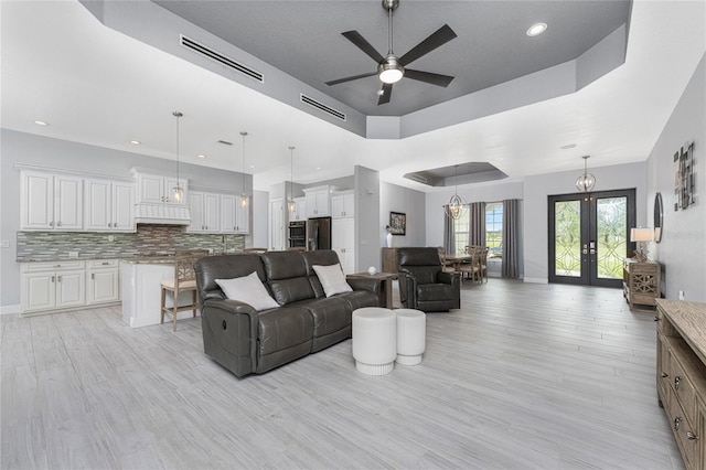 living room featuring ceiling fan, light wood-type flooring, french doors, and a tray ceiling