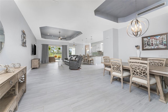 dining space with ceiling fan with notable chandelier, a raised ceiling, and light hardwood / wood-style flooring