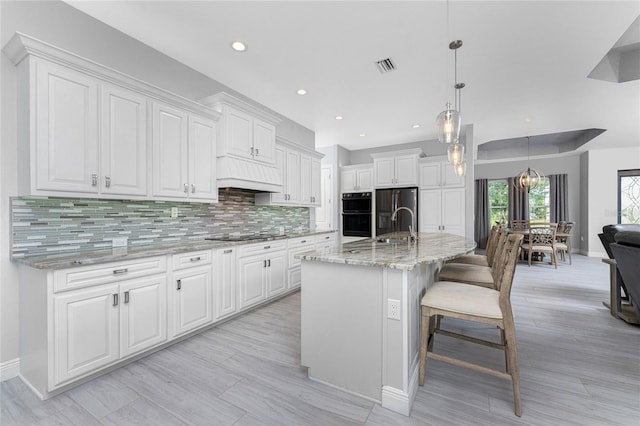 kitchen featuring decorative backsplash, light stone counters, white cabinets, decorative light fixtures, and a kitchen island with sink