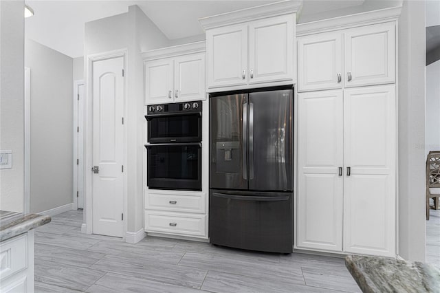 kitchen with light wood-type flooring, white cabinetry, light stone countertops, double oven, and stainless steel fridge