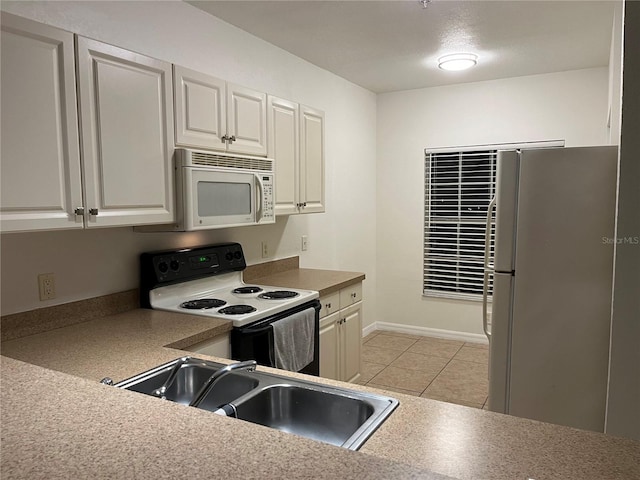 kitchen with white appliances, sink, light tile patterned floors, and white cabinetry