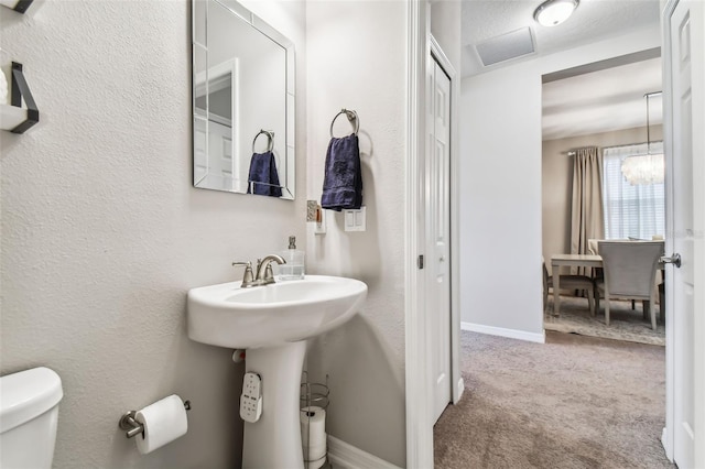 half bath with visible vents, baseboards, toilet, a textured wall, and a sink