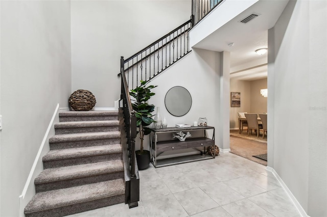 stairway featuring tile patterned floors, a high ceiling, baseboards, and visible vents