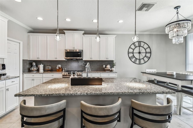 kitchen with decorative backsplash, stainless steel microwave, visible vents, and ornamental molding