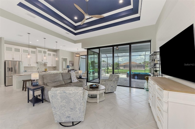 living room with a raised ceiling, sink, and ceiling fan