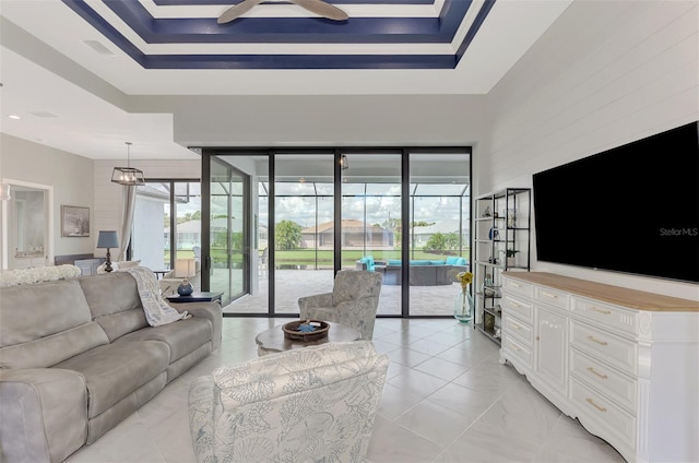 living room featuring ceiling fan with notable chandelier, a tray ceiling, and a healthy amount of sunlight