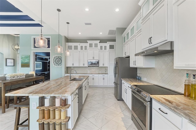 kitchen featuring appliances with stainless steel finishes, light stone counters, tasteful backsplash, pendant lighting, and a kitchen island with sink