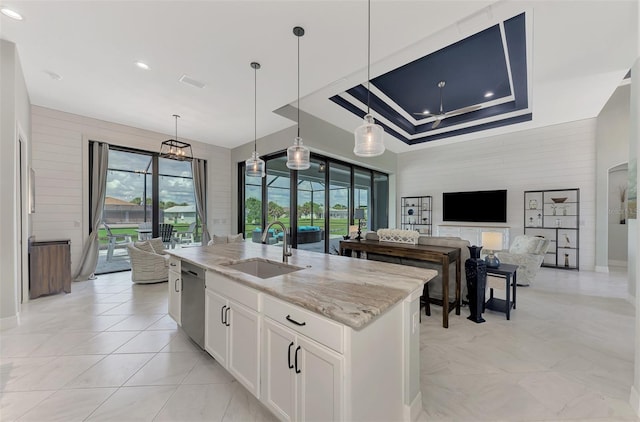 kitchen with light stone counters, dishwasher, a kitchen island with sink, sink, and white cabinetry