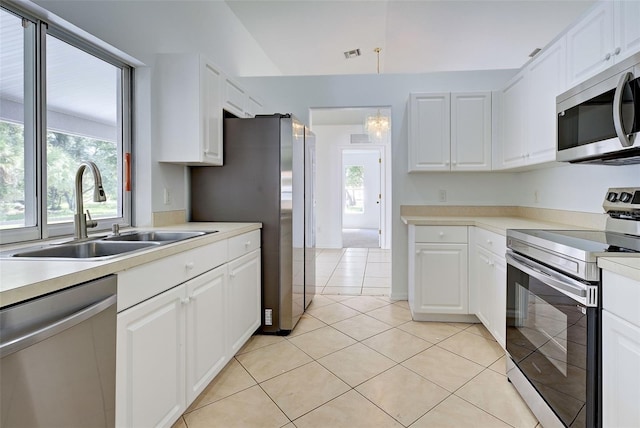 kitchen with light tile patterned floors, sink, white cabinetry, appliances with stainless steel finishes, and vaulted ceiling