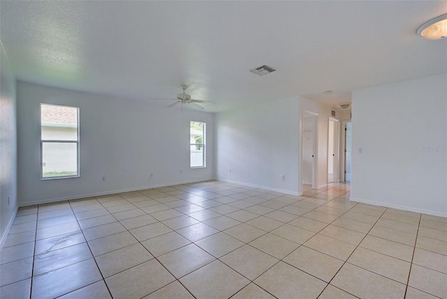 empty room with light tile patterned floors, ceiling fan, and a healthy amount of sunlight