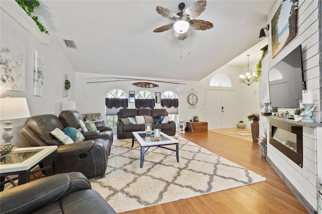 living room with ceiling fan with notable chandelier, wood-type flooring, and vaulted ceiling