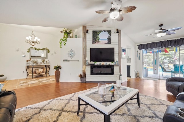 living room with ceiling fan with notable chandelier, lofted ceiling, hardwood / wood-style floors, and a large fireplace