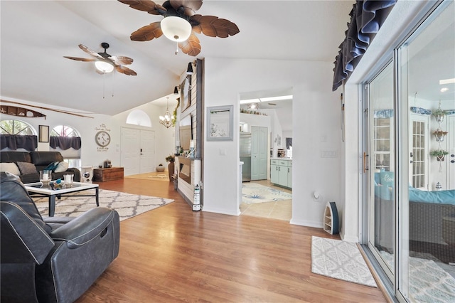 living room with ceiling fan with notable chandelier, lofted ceiling, and light hardwood / wood-style flooring