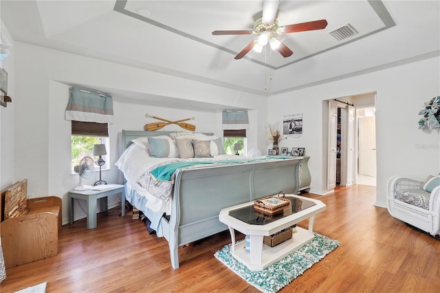 bedroom with a tray ceiling, multiple windows, hardwood / wood-style flooring, and ceiling fan