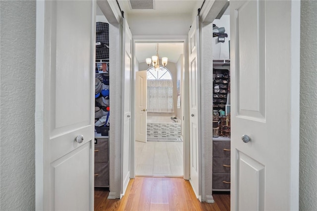 corridor with light hardwood / wood-style flooring and a notable chandelier