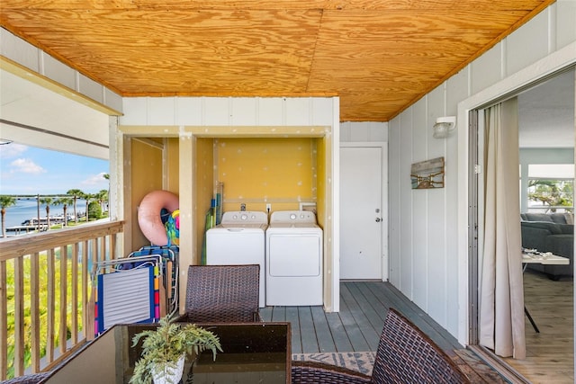 laundry room with wood ceiling, wood-type flooring, wood walls, a water view, and washing machine and dryer