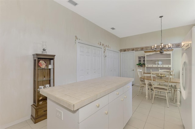 kitchen featuring white fridge, white cabinetry, tile countertops, decorative light fixtures, and a kitchen island