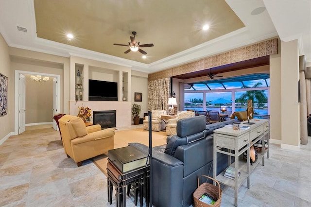 living room with ceiling fan with notable chandelier, a raised ceiling, crown molding, and built in features