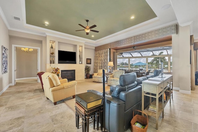 living room featuring ceiling fan with notable chandelier, built in shelves, ornamental molding, and a tray ceiling