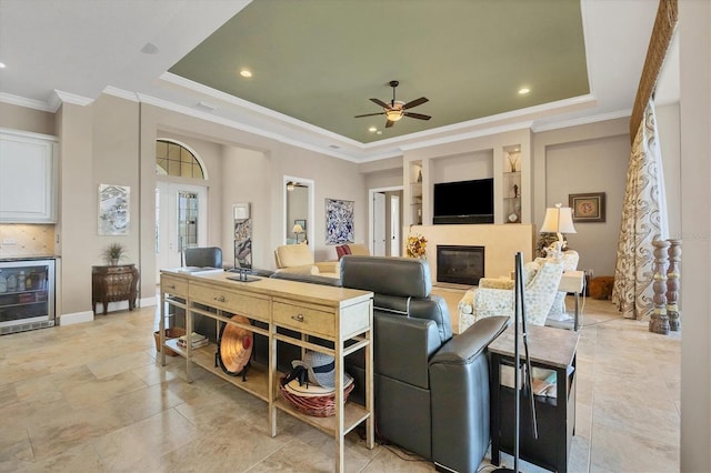 living room featuring ceiling fan, built in shelves, wine cooler, a tray ceiling, and crown molding