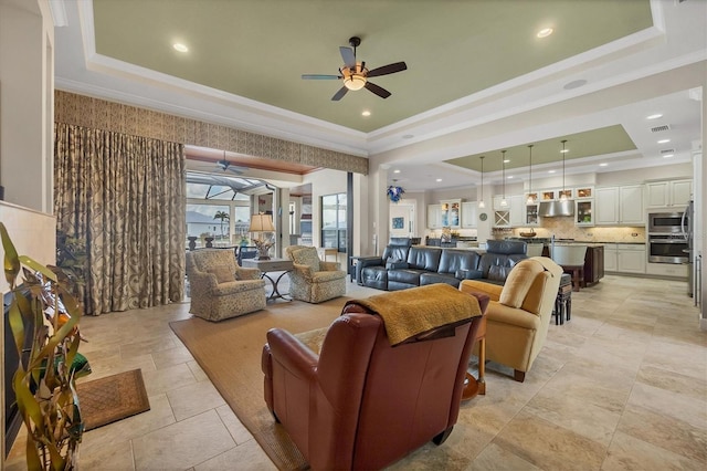 living room with ornamental molding, a tray ceiling, and ceiling fan