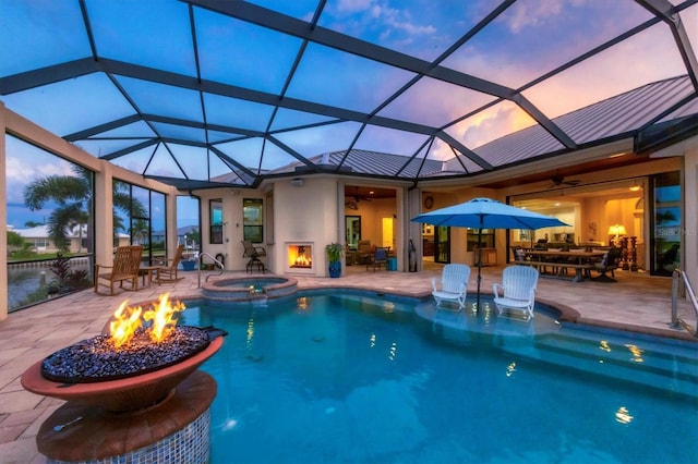 pool at dusk featuring a lanai, ceiling fan, an in ground hot tub, and a patio area