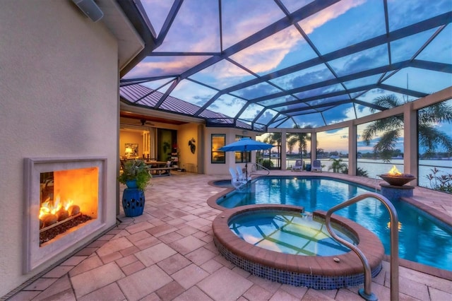 pool at dusk featuring a lanai, an in ground hot tub, and a patio area