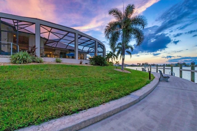 yard at dusk featuring a lanai and a water view