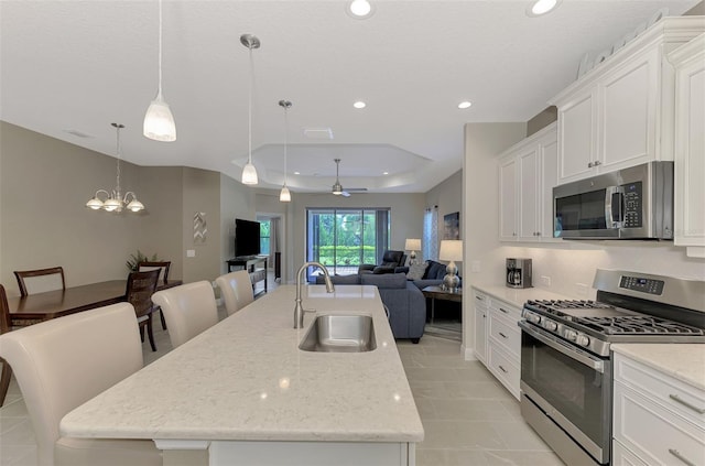 kitchen with hanging light fixtures, appliances with stainless steel finishes, sink, a kitchen island with sink, and a breakfast bar