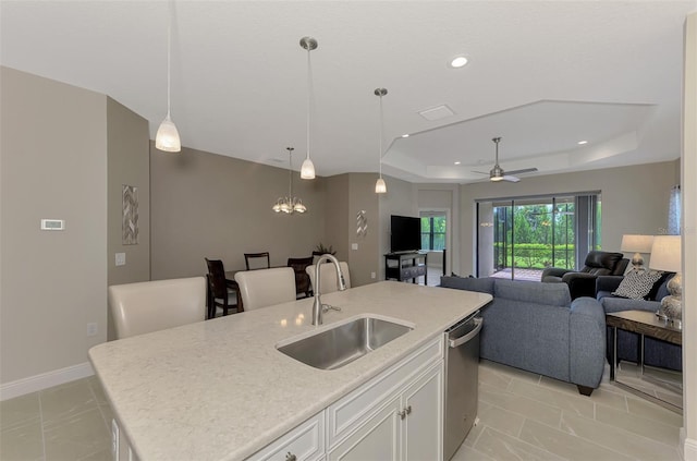 kitchen with dishwasher, ceiling fan with notable chandelier, white cabinetry, sink, and an island with sink