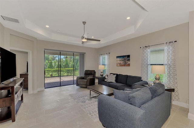 living room featuring a tray ceiling, ceiling fan, and light tile patterned floors