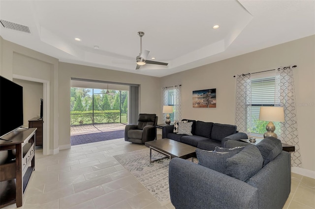 tiled living room with a raised ceiling and ceiling fan