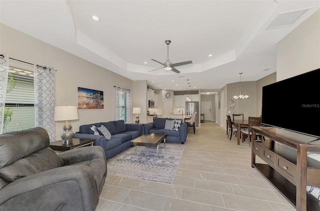 living room with ceiling fan with notable chandelier and a raised ceiling