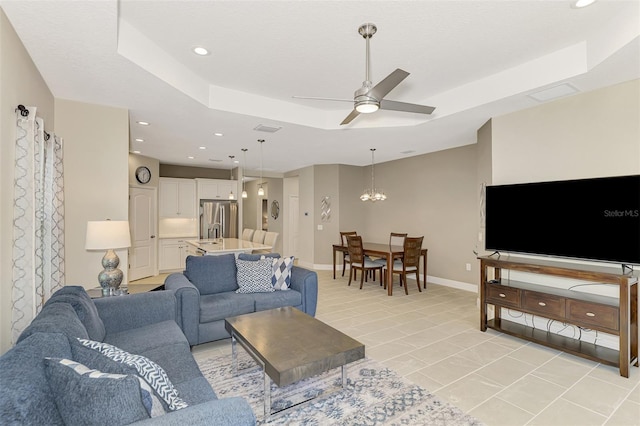 tiled living room featuring a raised ceiling and ceiling fan with notable chandelier