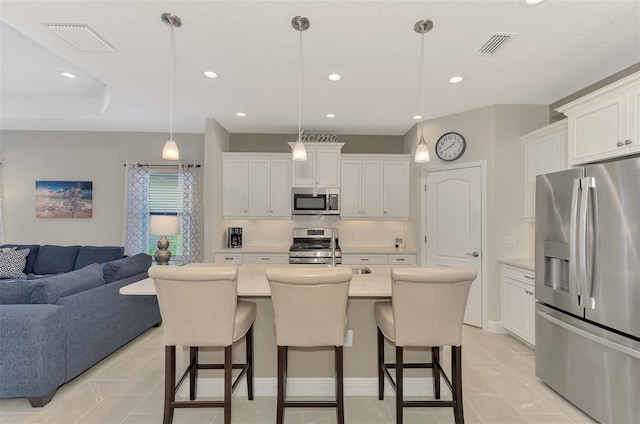 kitchen with a breakfast bar area, a center island with sink, pendant lighting, appliances with stainless steel finishes, and white cabinets