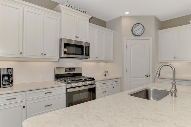 kitchen featuring appliances with stainless steel finishes, light stone countertops, white cabinetry, and sink