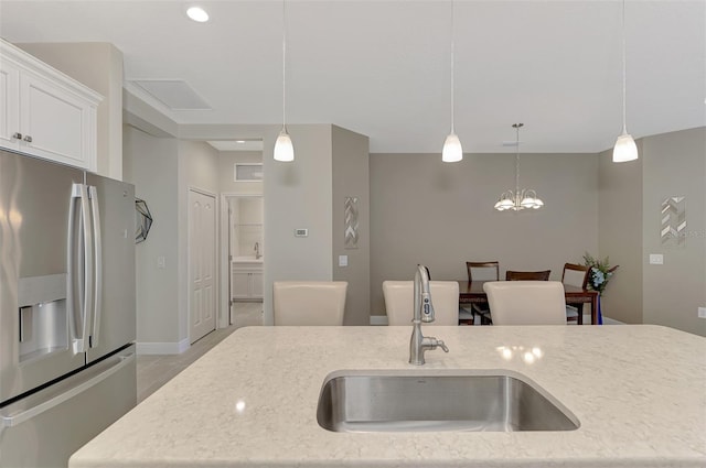 kitchen with light stone counters, decorative light fixtures, stainless steel fridge with ice dispenser, and sink