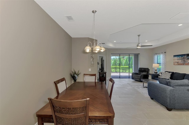 dining area with ceiling fan with notable chandelier and a tray ceiling