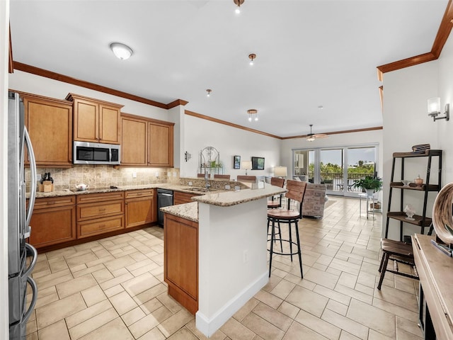 kitchen with kitchen peninsula, appliances with stainless steel finishes, light stone countertops, a kitchen bar, and decorative backsplash