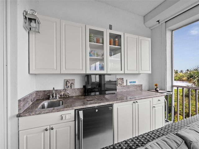 kitchen featuring stainless steel fridge, dark stone countertops, white cabinetry, and sink