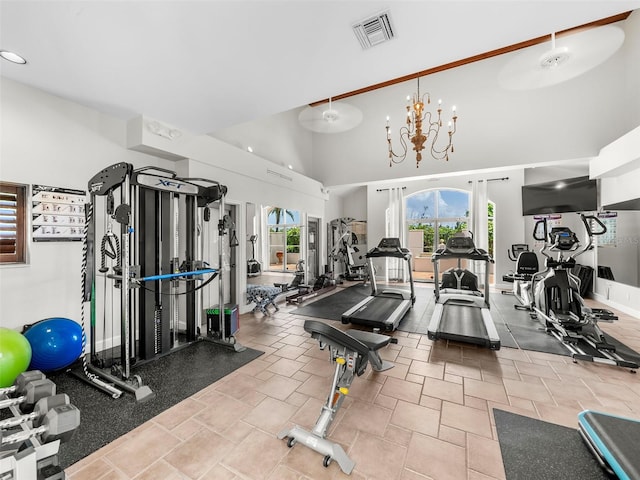 gym featuring a towering ceiling and a chandelier