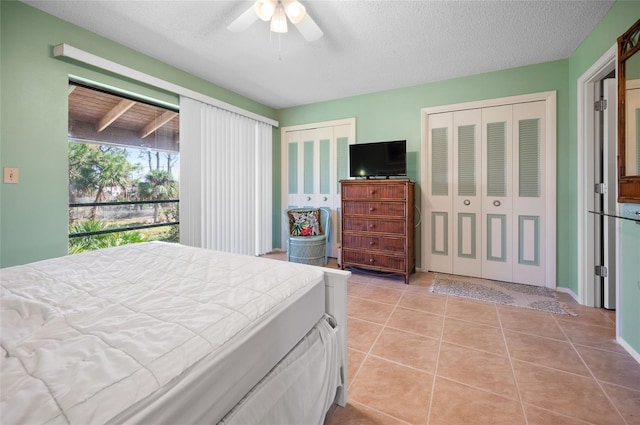 bedroom with multiple closets, light tile patterned flooring, a textured ceiling, and ceiling fan