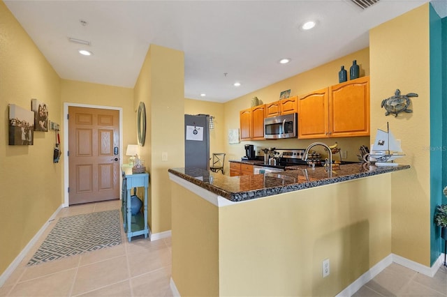 kitchen featuring dark stone counters, stainless steel appliances, kitchen peninsula, and light tile patterned flooring