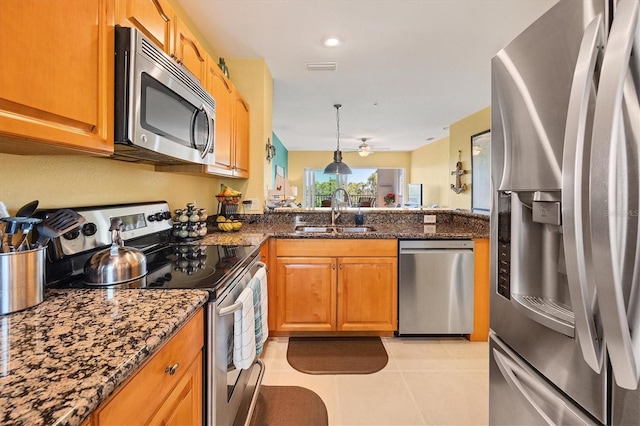 kitchen featuring light tile patterned flooring, sink, decorative light fixtures, stainless steel appliances, and dark stone countertops