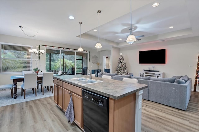 kitchen featuring a healthy amount of sunlight, ceiling fan with notable chandelier, a tray ceiling, black dishwasher, and a kitchen island with sink