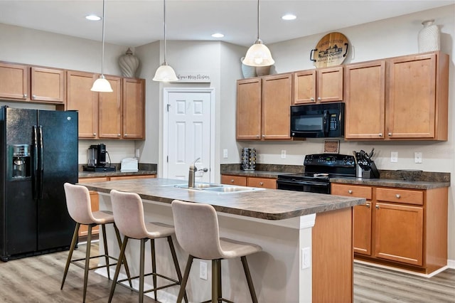 kitchen featuring black appliances, decorative light fixtures, light wood-type flooring, and a kitchen island with sink