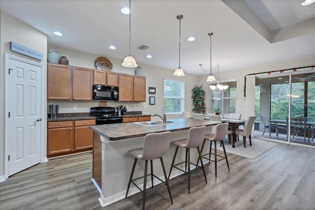 kitchen featuring black appliances, pendant lighting, a kitchen bar, sink, and a chandelier